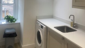 A compact kitchen with a skylight, a washing machine, and a sink. - Central Paisley Apartment- Airport/glasgow Access (Paisley)