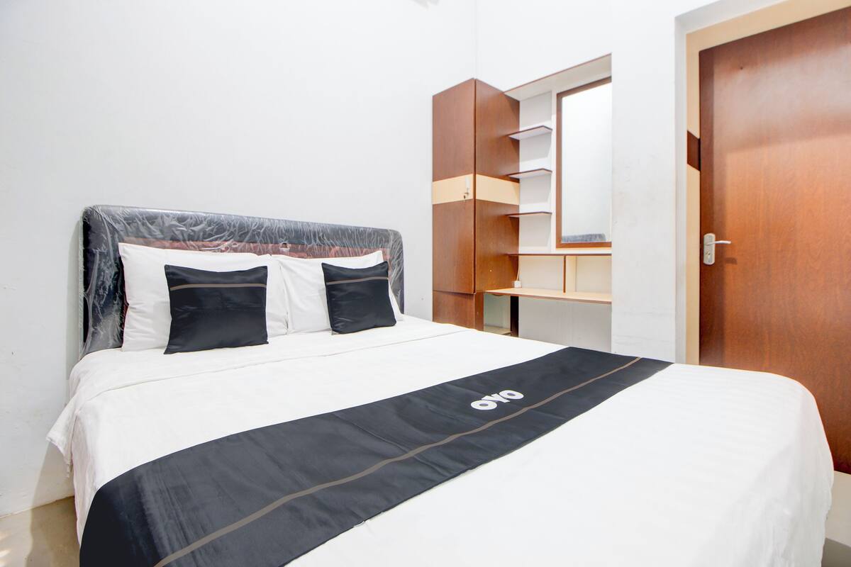 Cama bem arrumada com colcha preta e branca, cabeceira de madeira e espelho sobre um guarda-roupa de madeira.