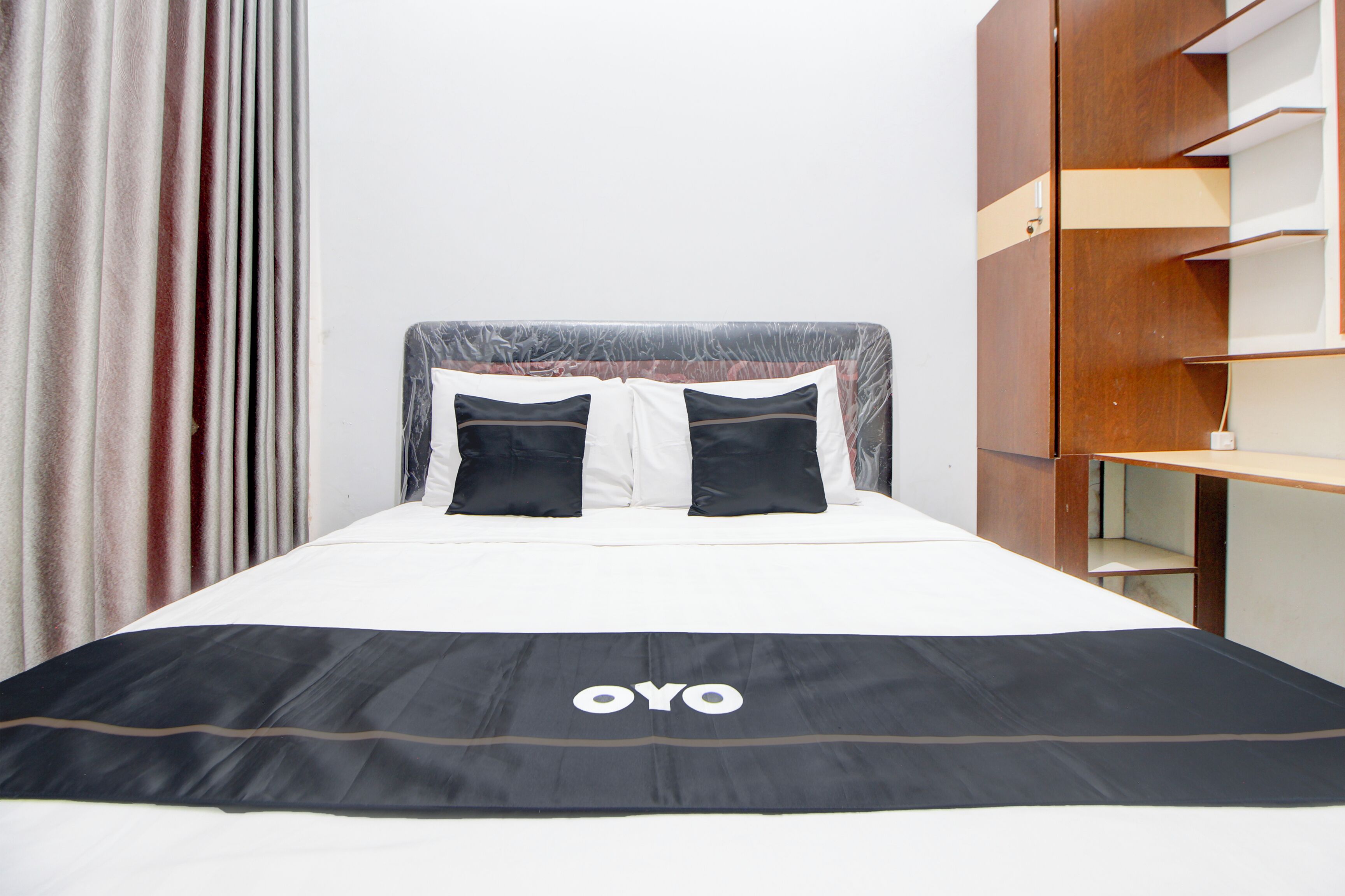 Una cama con colcha blanco y negro, dos almohadas negras y cabecera con diseño estampado.