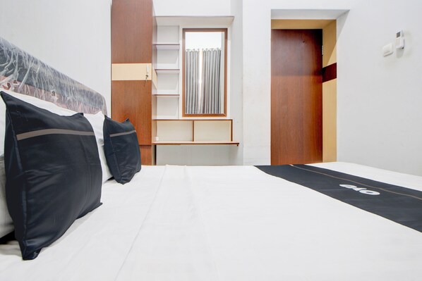 A modern bedroom with a bed, pillows, a desk, and a window.