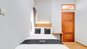 A neatly made bed with a black and white bedspread and a logo, a wooden door, a small window, and a light switch on the wall. - Capital O 94314 Sunny Co Living (Banguntapan)