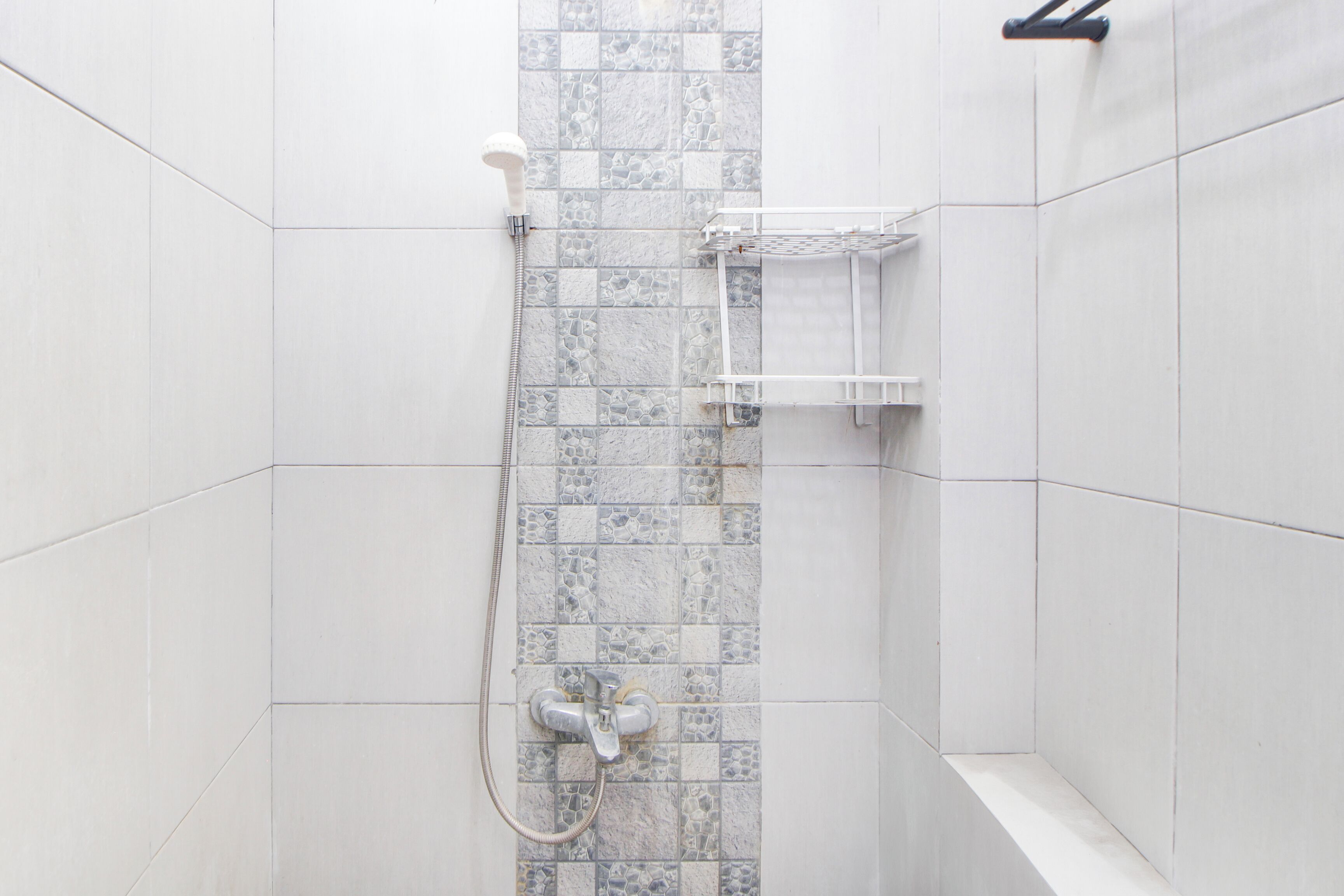 Zona de ducha con pared de azulejos, cabezal de ducha y estante.