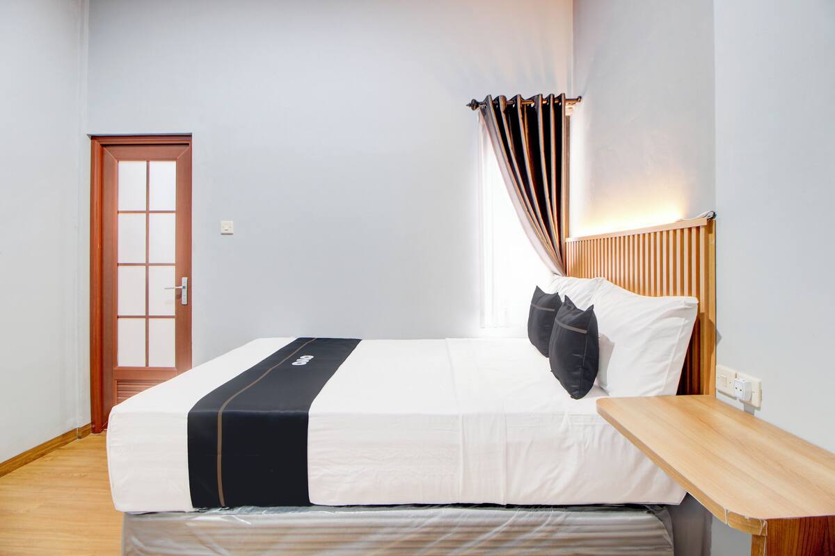Cama bem arrumada com cabeceira de madeira, mesa de cabeceira e porta com painel de vidro jateado.