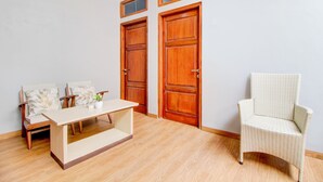 A room with a wooden floor, a small table, two chairs, and two wooden doors. - Capital O 94314 Sunny Co Living (Banguntapan)