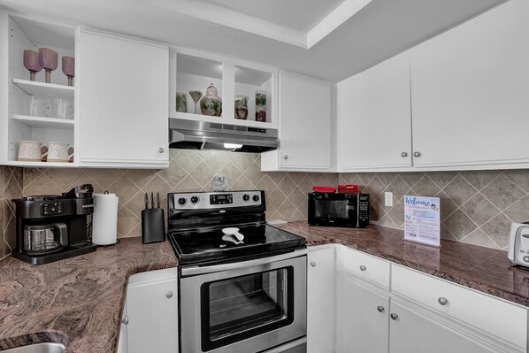 A modern kitchen with white cabinets, a black stove, a microwave, and a coffee maker.