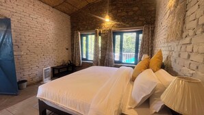 A room with a bed, a lamp, a window with curtains, and a stone wall. - Burans Kot Heritage Home - Ramgarh (Kosiyakutoli)