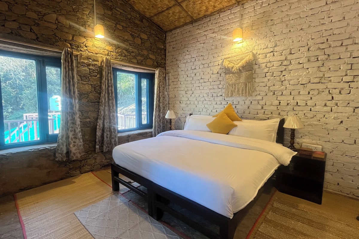 A bedroom with a stone wall, a bed with white bedding, and two bedside lamps.