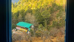 A view of a green-roofed building with a signboard, surrounded by a hilly landscape with a rainbow in the sky. - Burans Kot Heritage Home - Ramgarh (Kosiyakutoli)