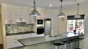 Una cocina moderna con armarios blancos, un refrigerador de acero inoxidable, un microondas y un lavamanos doble.