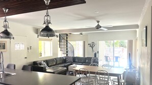 Una cocina moderna con una isla central, un comedor con sillas blancas, un sofá de cuero negro y una escalera que sube a otro nivel.