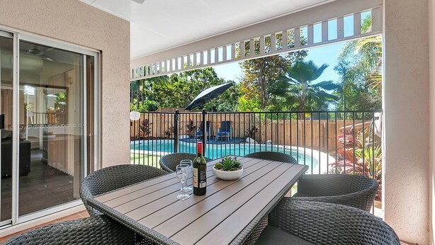 Un balcón con piscina, muebles de mimbre y una botella de vino.