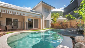 Una piscina con hidromasaje, rodeada por una casa con patio y valla de madera.