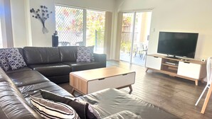Una sala de estar moderna con un sofá de cuero, una mesa de centro de madera y un televisor de pantalla plana sobre un mueble de madera.