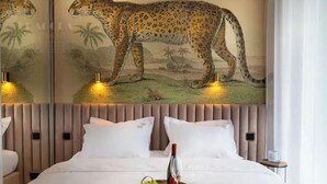 Ein Hotelzimmer mit einer großen Leopardenmalerei an der Wand, einem Bett mit weißen Leinentüchern und einem Tablett mit Trauben und einer Weinflasche.