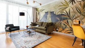 Ein Wohnzimmer mit einer Couch, einem Couchtisch, einem gelben Sessel und einem großen Wandgemälde von Katzen.