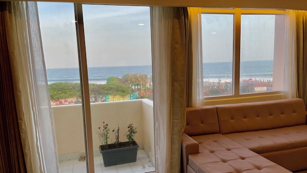 A room with a large sliding glass door leading to a balcony with a view of the sea and a beach. - Ocean's Edge by Natti's group (Visakhapatnam)