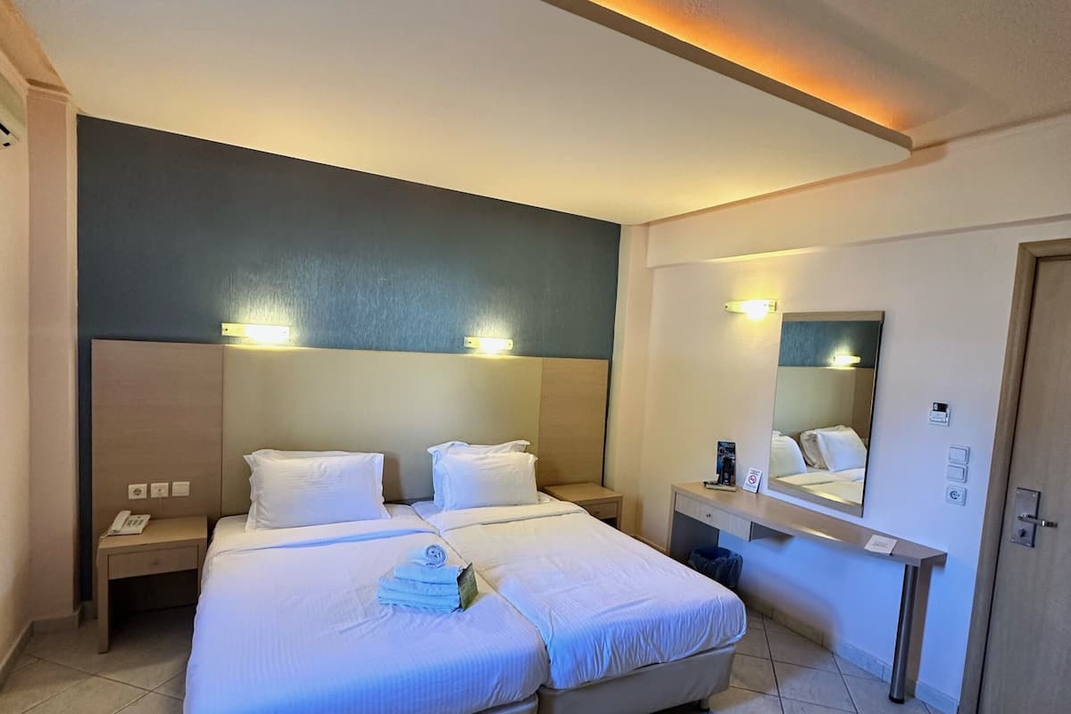 A hotel room with two beds, a bedside table with a phone, a mirror, and a small desk with a chair.