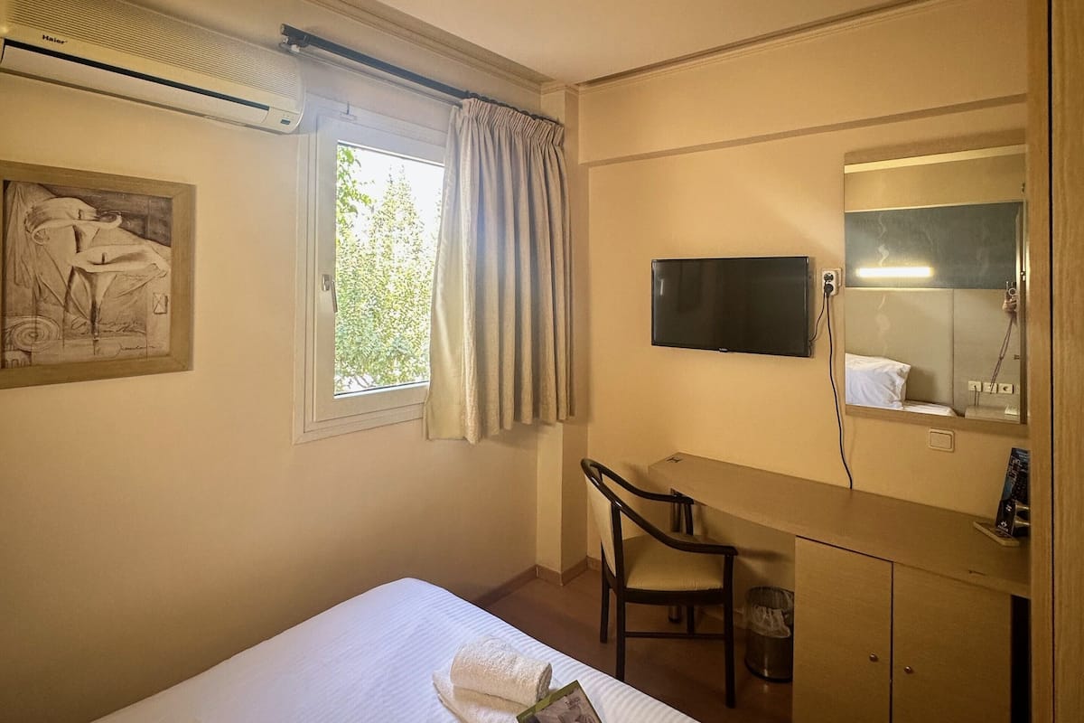 A hotel room with a bed, a desk, a chair, a television, and a wardrobe.