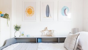A bedroom with a bed, a bedside table, a wall-mounted shelf, and three framed artworks depicting a sun, a surfboard, and a crescent moon.