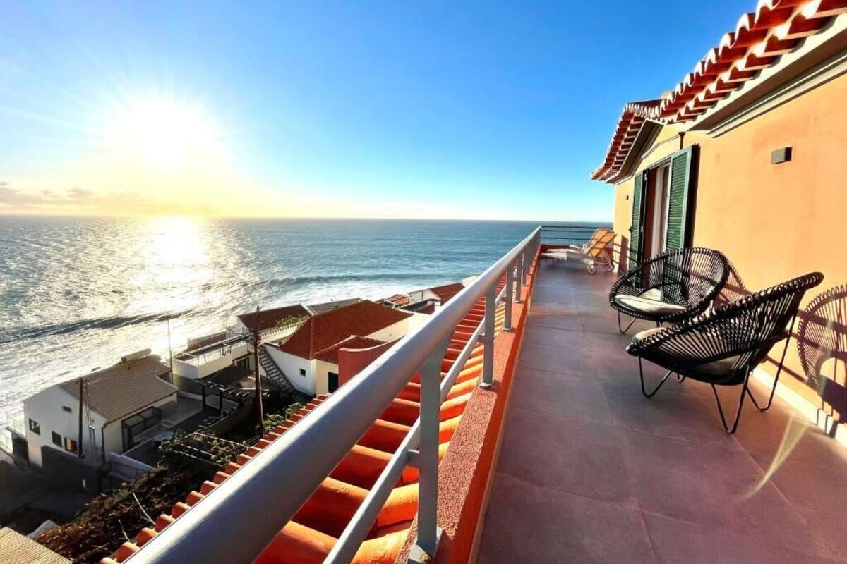 A balcony with a view of the ocean, a staircase, and outdoor seating.