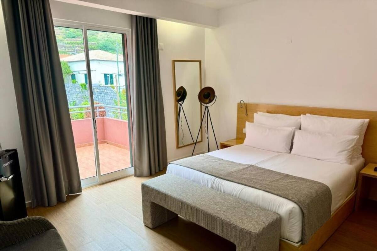 A hotel room with a large bed, a bench, a desk, and a view of the outside.