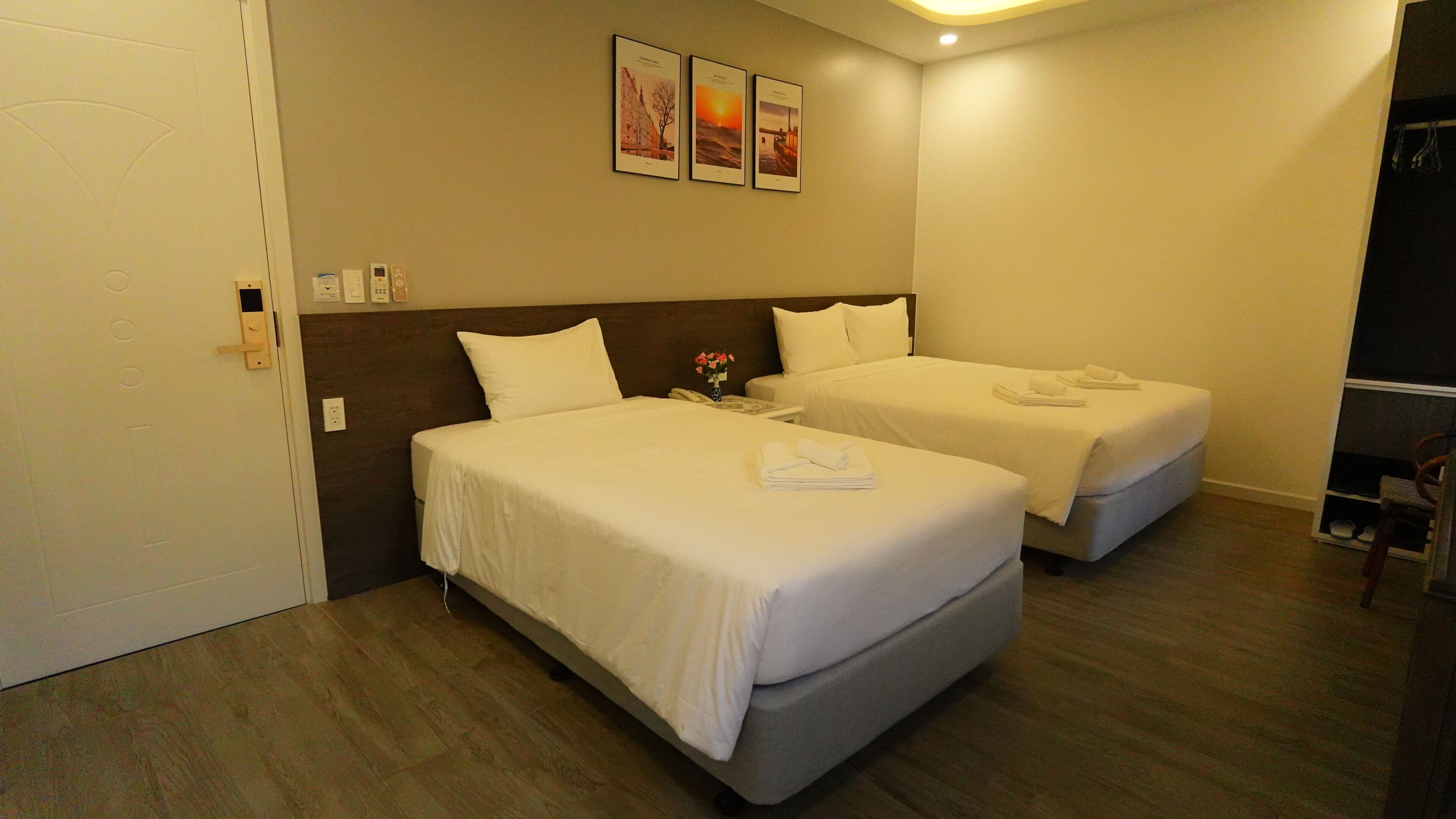 A hotel room with two beds, a nightstand, a vase with flowers, and three framed pictures on the wall.