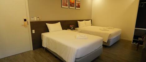 A hotel room with two beds, a nightstand, a vase with flowers, and three framed pictures on the wall.