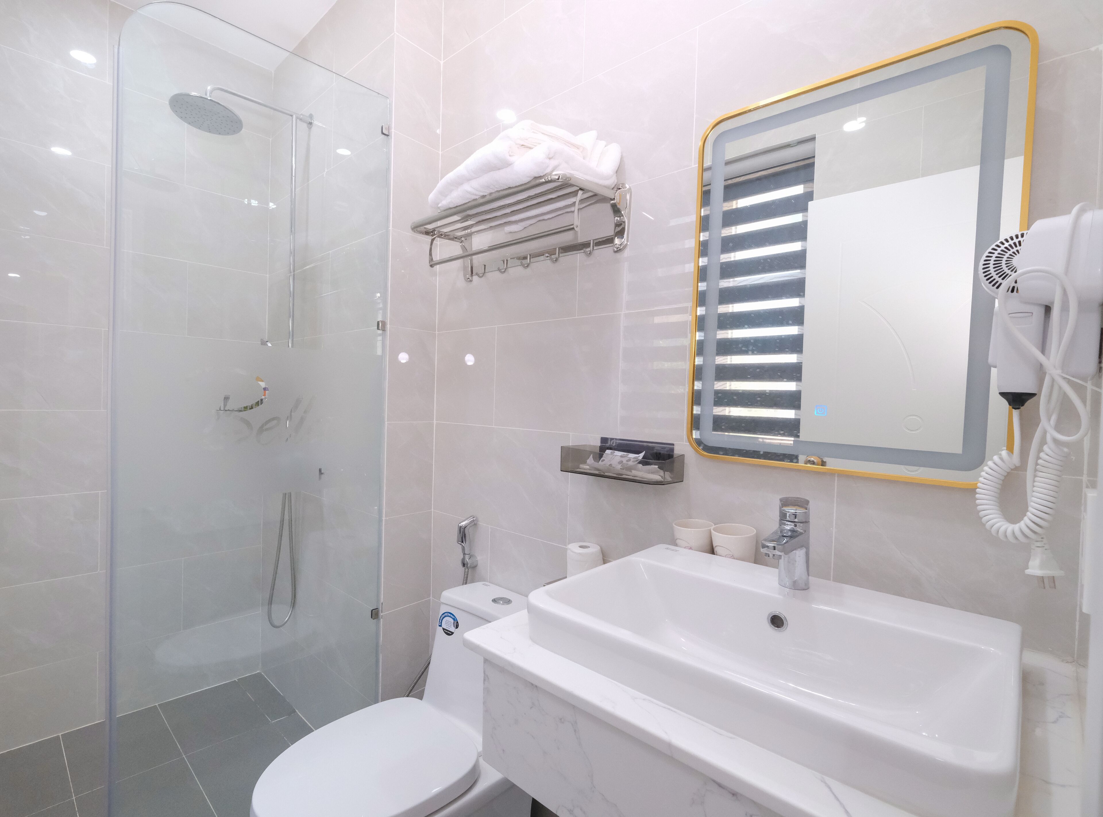 Un baño moderno con ducha de vidrio, lavamanos blanco y espejo con marco dorado.