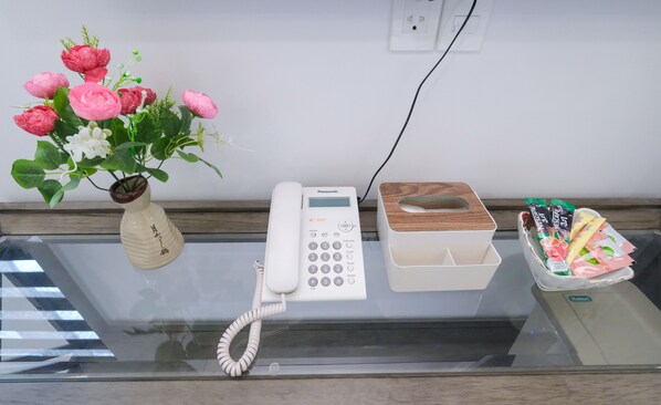 Une table en verre sur laquelle se trouvent un téléphone Panasonic blanc, un vase avec des fleurs roses et une boîte de mouchoirs.