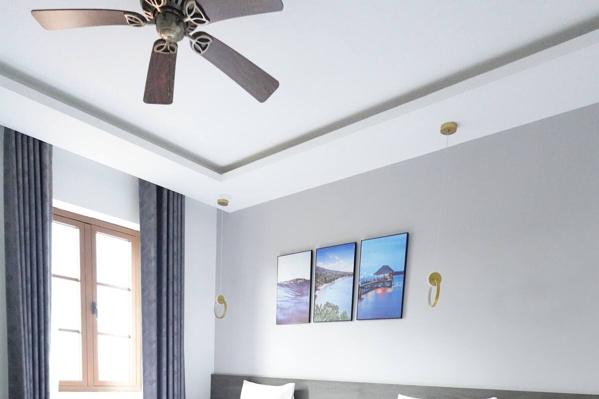 Une chambre d’hôtel avec deux lits, un ventilateur de plafond, une fenêtre avec des rideaux et des œuvres d’art accrochées au mur.