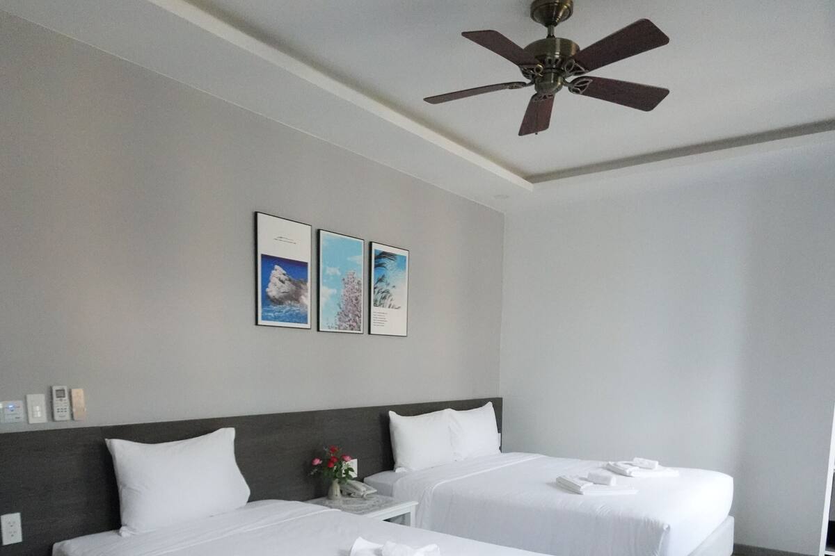 Une chambre d’hôtel avec deux lits, un ventilateur de plafond et des tableaux encadrés accrochés au mur.
