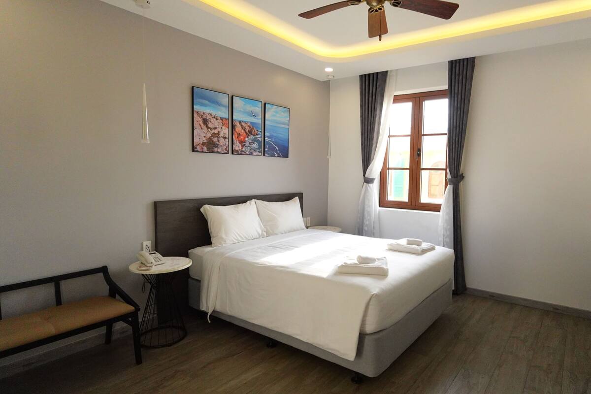 Une chambre d’hôtel équipée d’un lit, d’une table de chevet, d’un banc et d’un ventilateur de plafond.