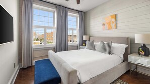 Een moderne hotelkamer met een groot bed, een plafondventilator, een televisie en uitzicht op de stad.