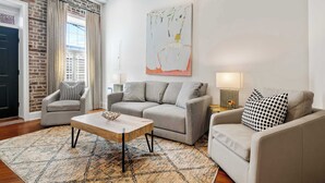 Un salon avec un canapé, des fauteuils, une table basse et un tableau au mur.
