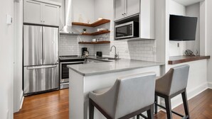 Une cuisine moderne avec des meubles blancs, un réfrigérateur en acier inoxydable, un four à micro-ondes et un coin bar équipé de deux tabourets.