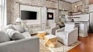 A modern living room with a sofa, armchairs, and a TV mounted on a brick wall.