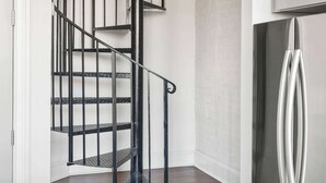 A kitchen with a stainless steel refrigerator, a wooden countertop, and a black spiral staircase.