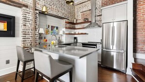 A modern kitchen with a large island, stainless steel appliances, and exposed brick walls.