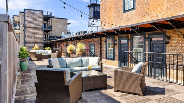 A rooftop patio with wicker furniture, a brick building, and a metal staircase.