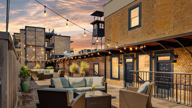 An outdoor seating area with wicker furniture, string lights, and a brick building in the background. - Perfect Location - King Street Condo! (Charleston)