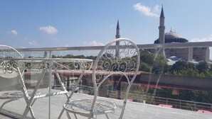 Ein Balkon mit Metallstühlen und einem Tisch, mit Blick auf eine Moschee mit zwei Minaretten und einer Kuppel.