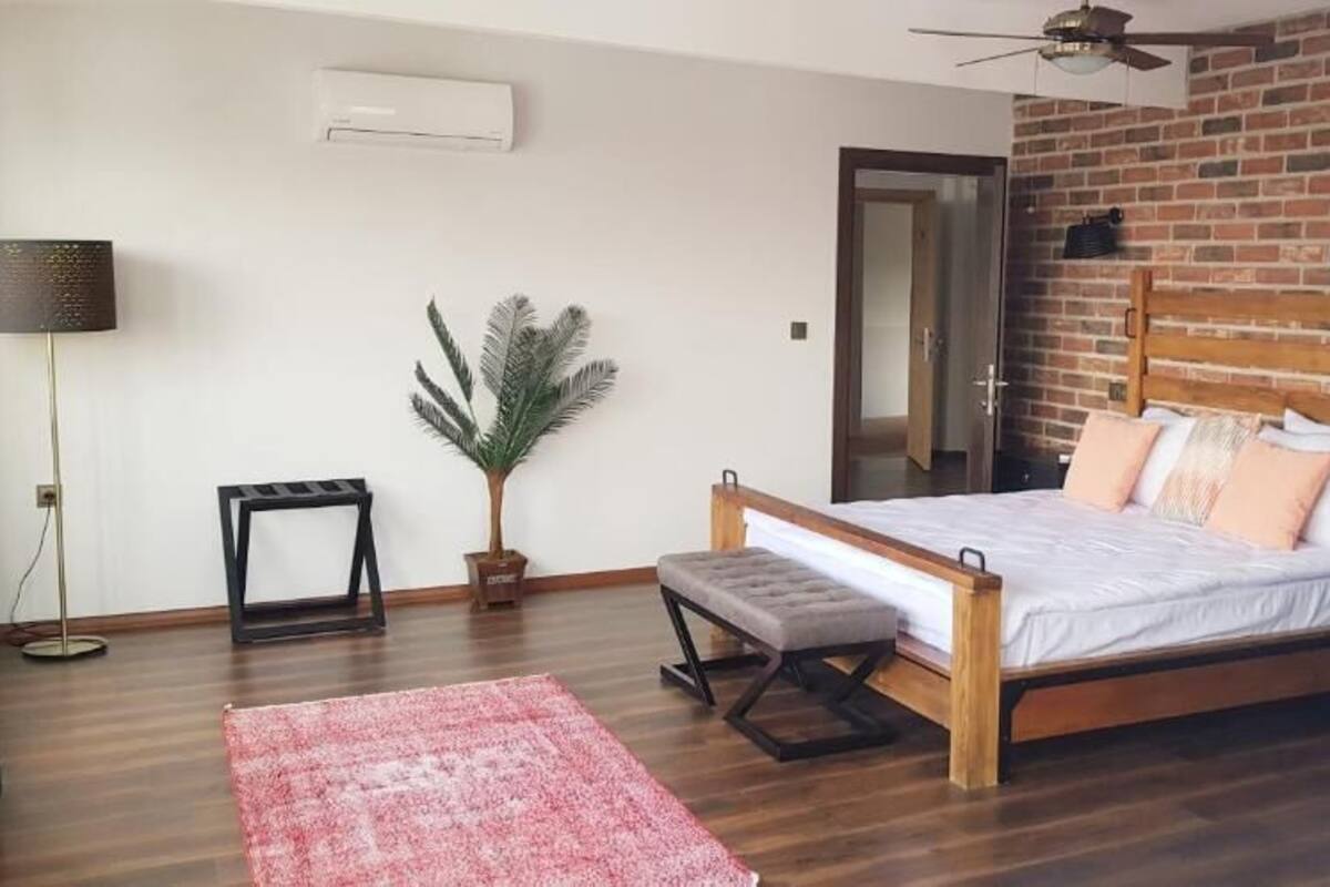 Une chambre à coucher avec un lit en bois, un petit banc, une plante en pot, une lampe sur pied et un tapis rouge.