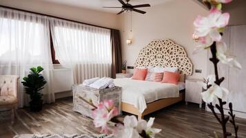 Un dormitorio con cama, ventilador de techo, mesita de noche, planta en maceta, silla y un adorno en la pared.
