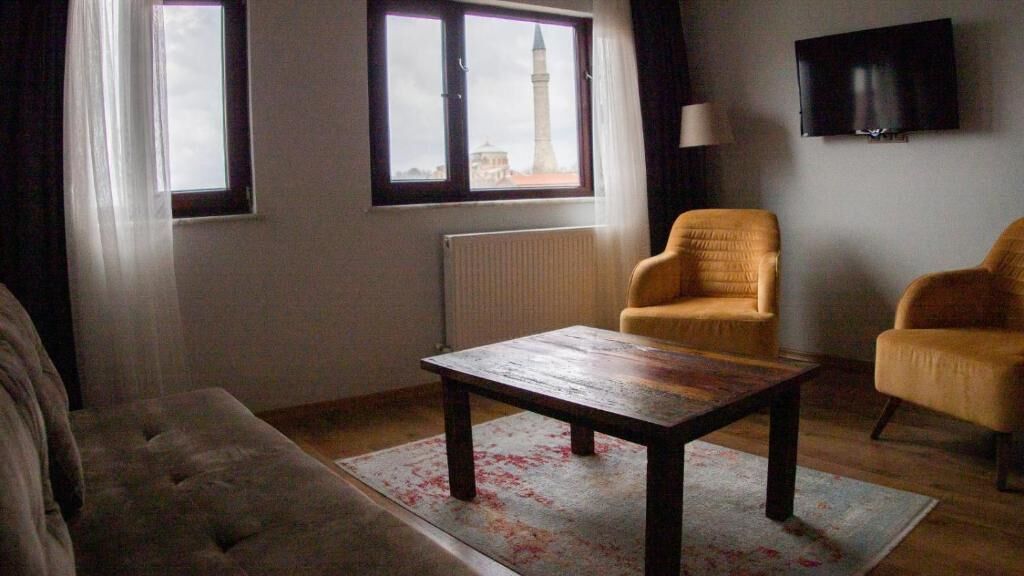 Sala de estar com mesa de centro de madeira, duas poltronas, um sofá, um radiador e uma janela com vista para uma torre.