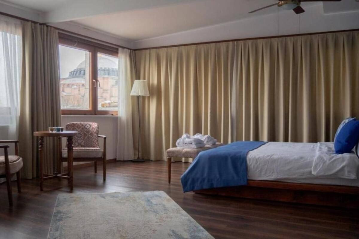 Une chambre d’hôtel avec un lit, une chaise, une petite table et une vue sur un immeuble par la fenêtre.