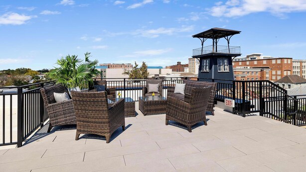 A rooftop terrace with wicker furniture, a small table, and a view of the cityscape. - Fire Tower | King Street Condo - Walk Everywhere! (Charleston)