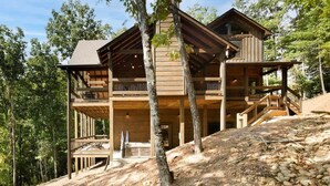 A two-story wooden cabin with a balcony on the upper level, surrounded by trees. - Luxury Cabin w/ Stunning Mountain Views & Hot Tub (Blue Ridge)