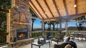 A covered outdoor seating area with stone walls, a fireplace, and a view of the surrounding landscape. - Luxury Cabin w/ Stunning Mountain Views & Hot Tub (Blue Ridge)