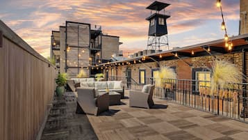 A rooftop patio with outdoor seating, string lights, and a view of the cityscape during sunset.