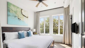 Un dormitorio amplio con una cama grande, ventilador de techo, televisor y ventana con cortinas.